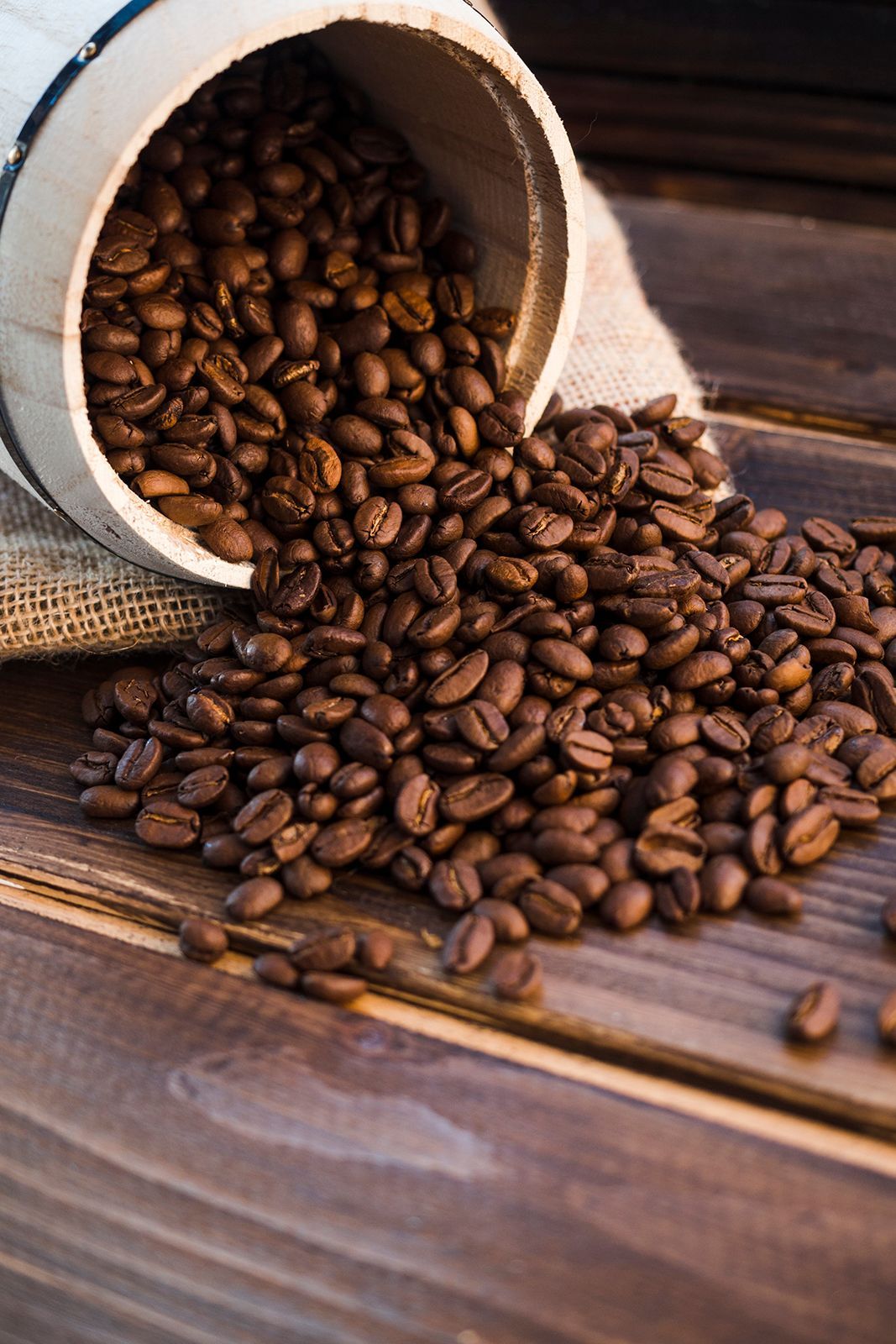 Granos de café tostados derramándose de un barril de madera sobre una mesa de madera.