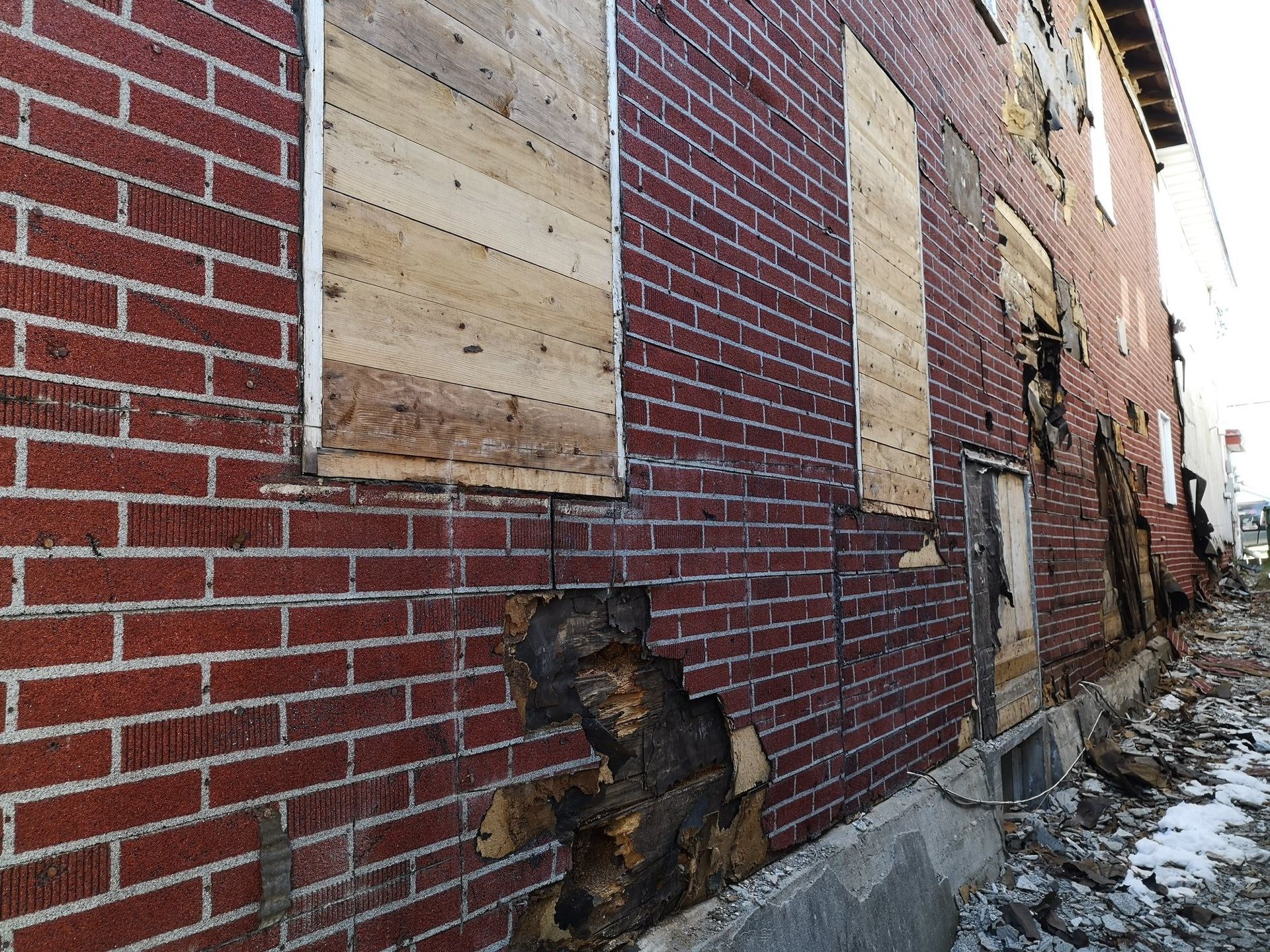 Un bâtiment en briques avec des planches de bois sur les fenêtres est en train d'être démoli.