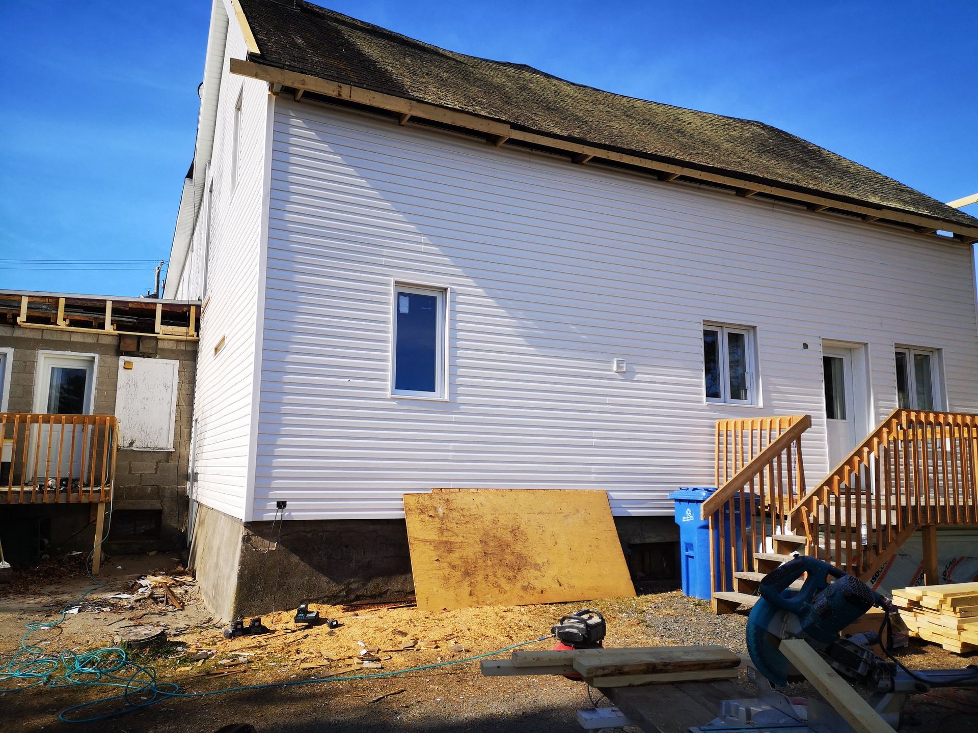 Une maison blanche avec des escaliers et une poubelle bleue devant