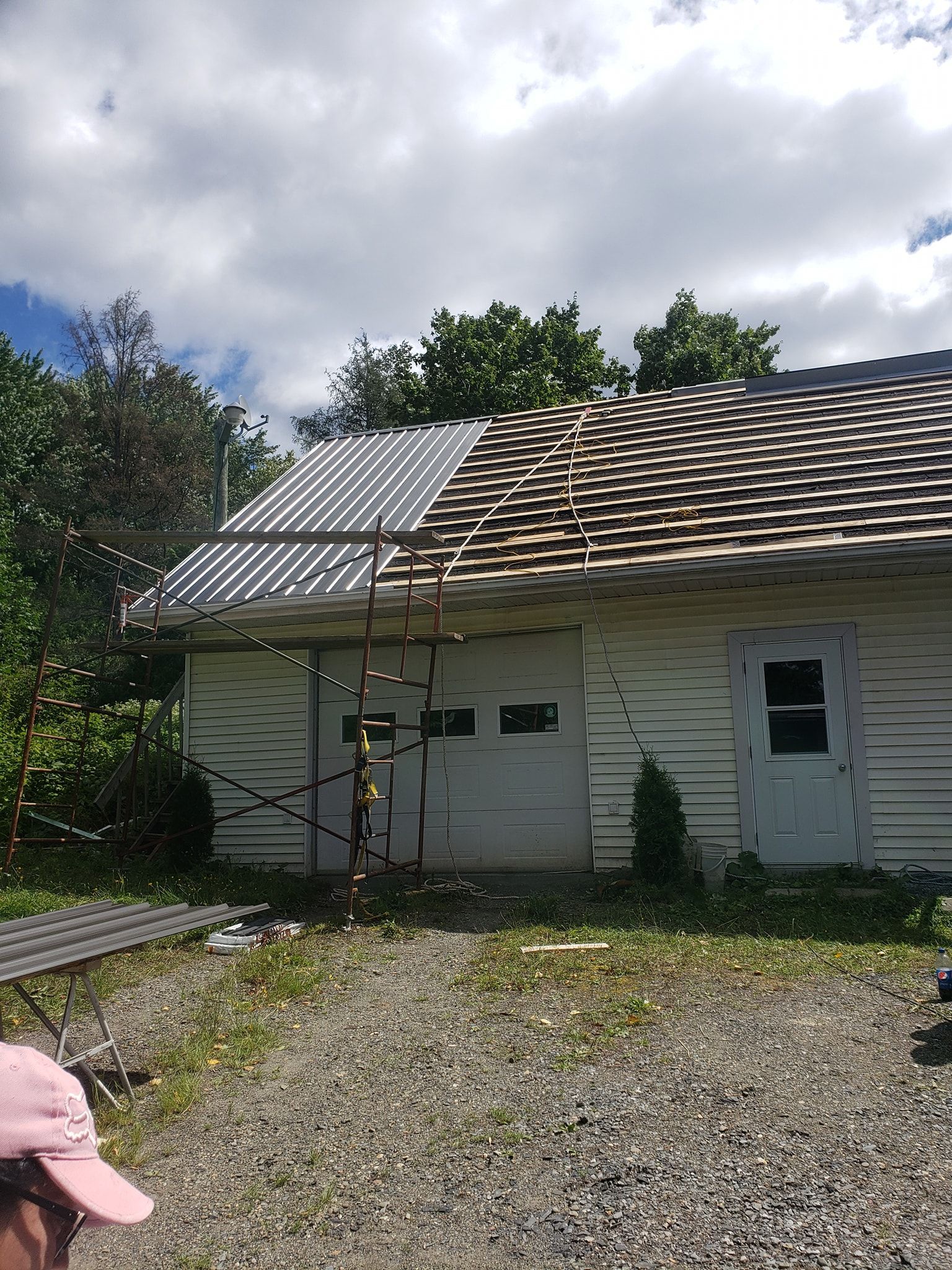 Un homme se tient devant une maison blanche dont le toit est en cours de réparation.