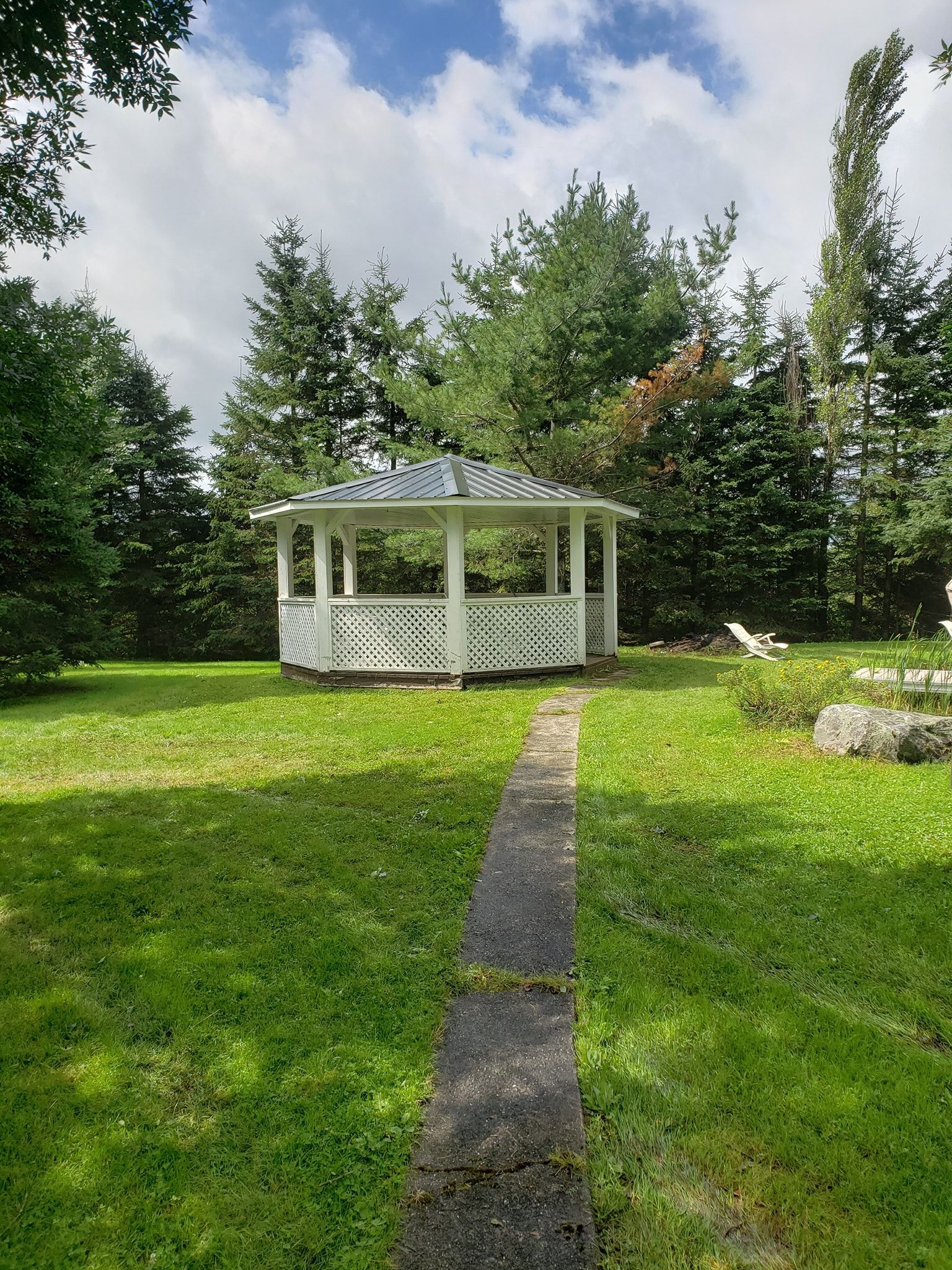 Un belvédère blanc est assis au milieu d'un champ vert luxuriant entouré d'arbres.