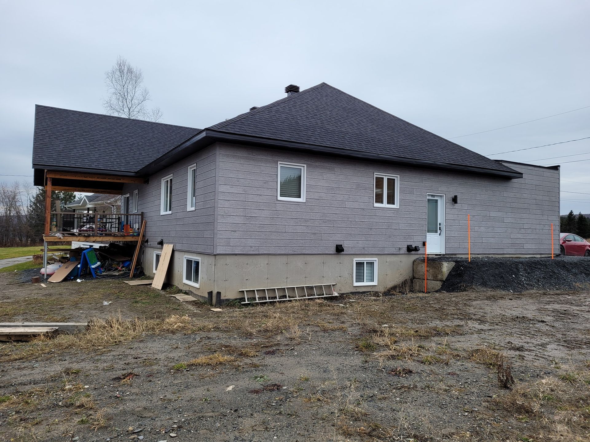 Une grande maison en briques avec un toit noir est en construction dans un champ de terre.