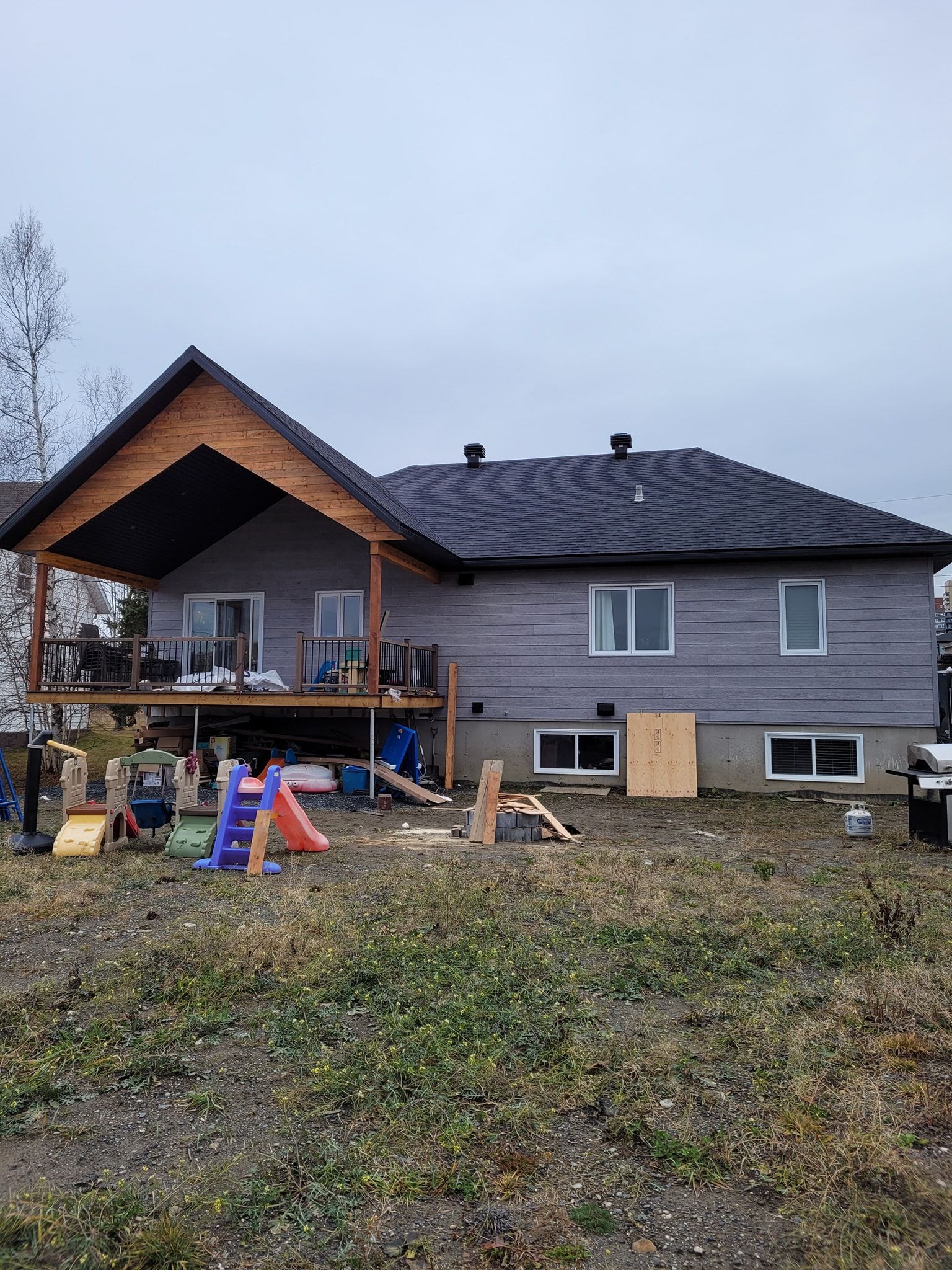 Une grande maison avec une terrasse et une aire de jeux devant.