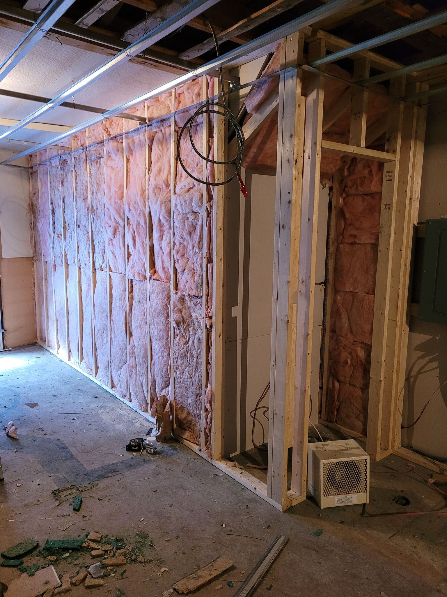 Une pièce avec un mur en construction et un ventilateur au sol.