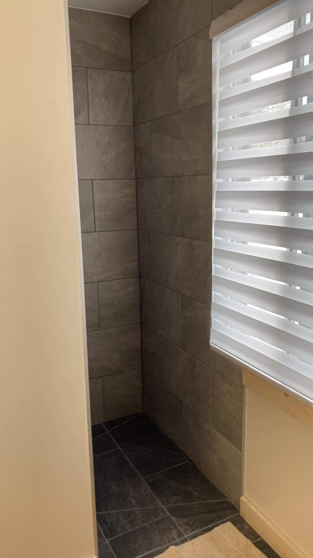 Une salle de bain avec douche à l'italienne et une fenêtre avec stores.