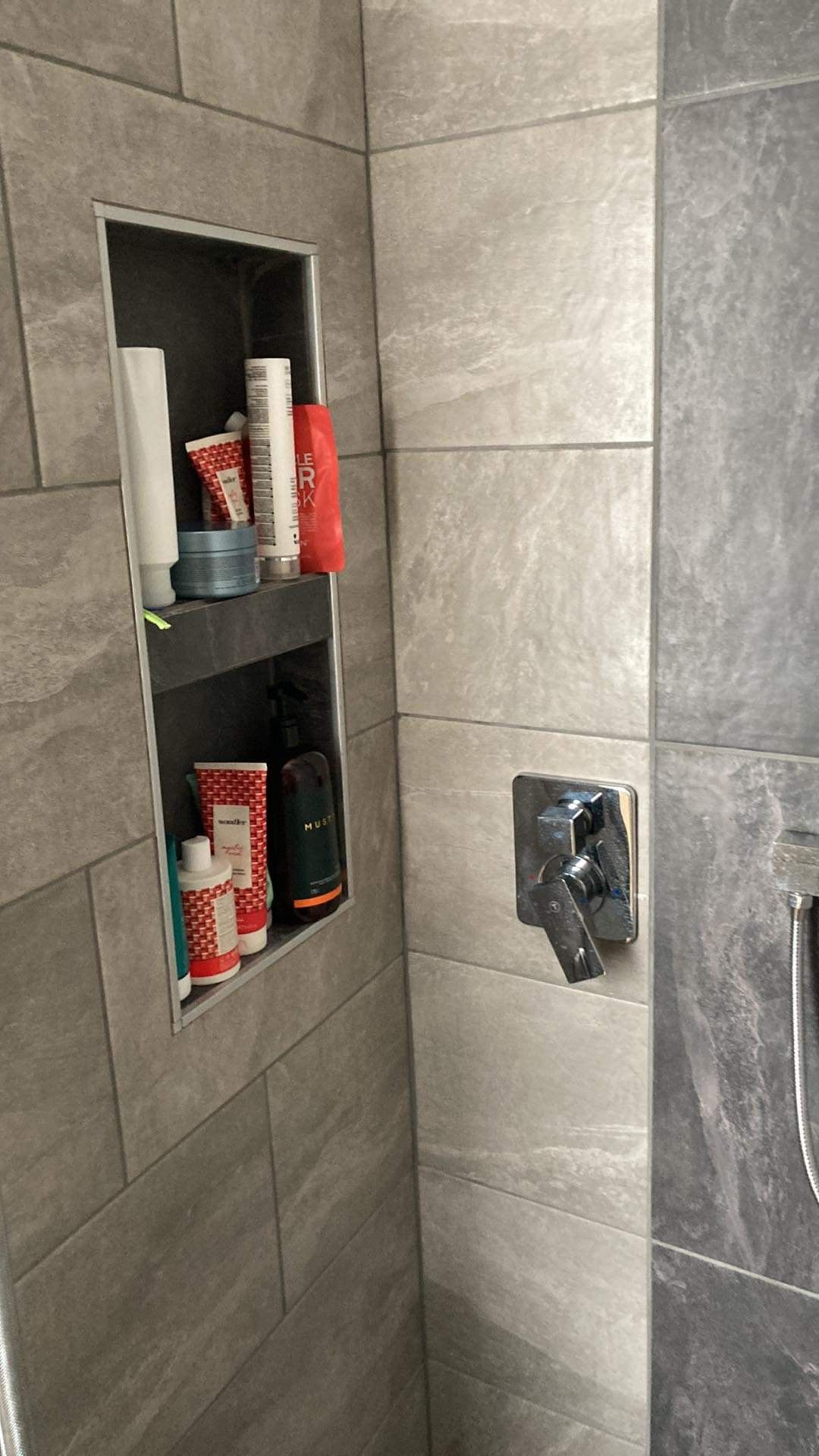 Une douche avec une étagère intégrée et un pommeau de douche.