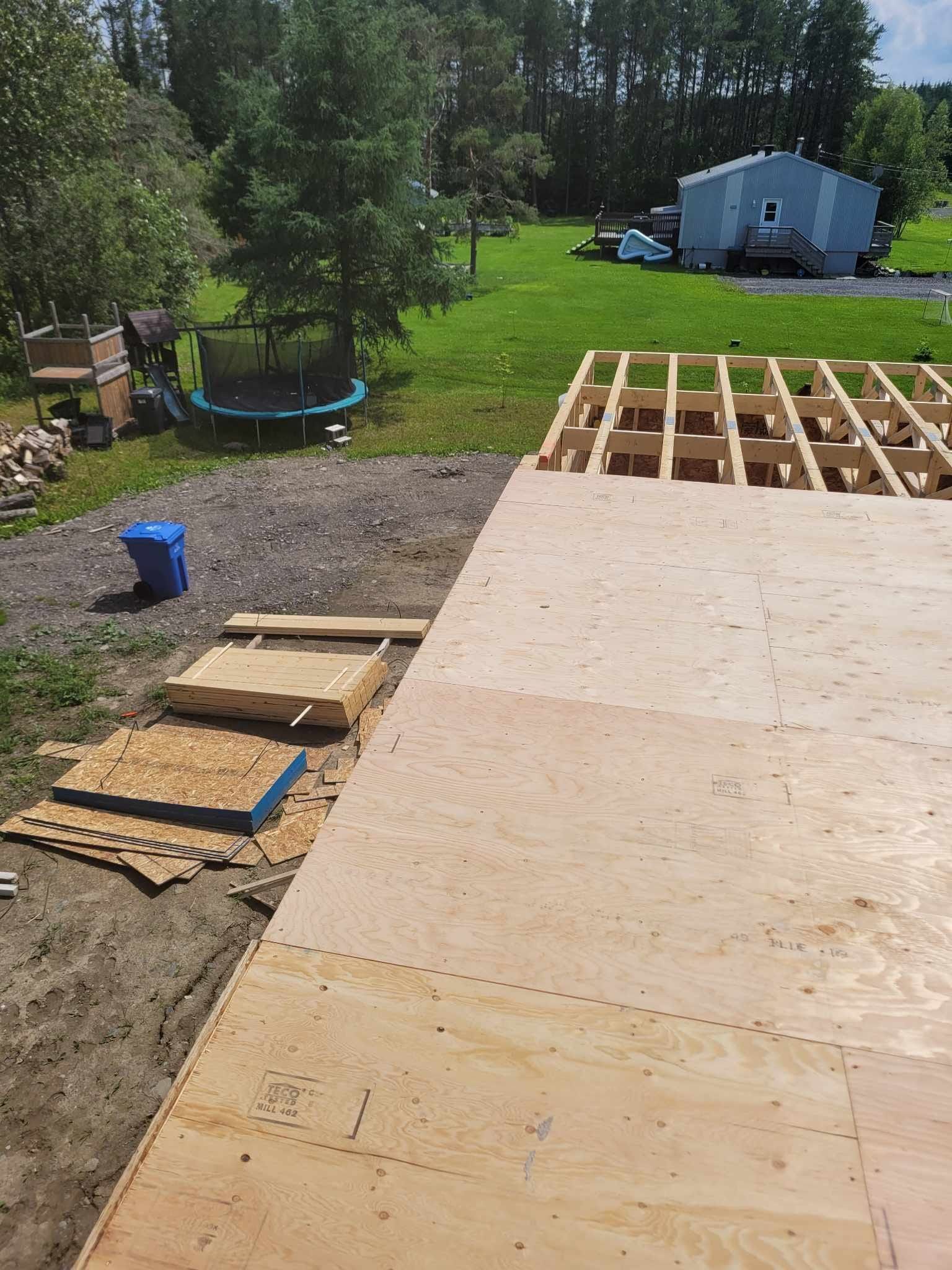 Une terrasse en bois est en cours de construction dans une cour arrière avec un trampoline en arrière-plan.