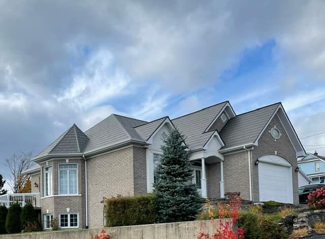 Une grande maison avec un toit gris est assise au sommet d'une colline.