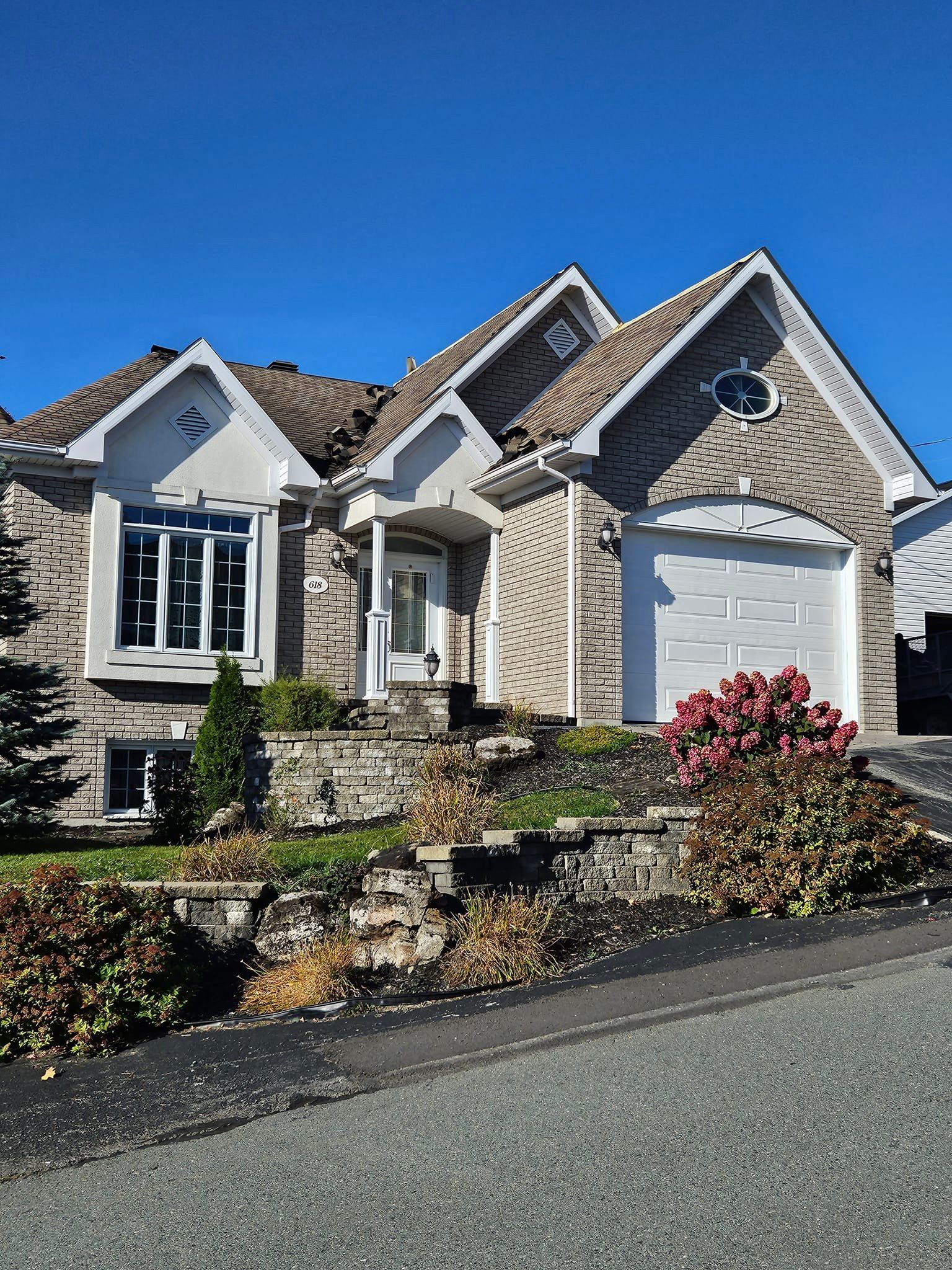 Une grande maison en briques avec une porte de garage blanche est assise au sommet d'une colline.