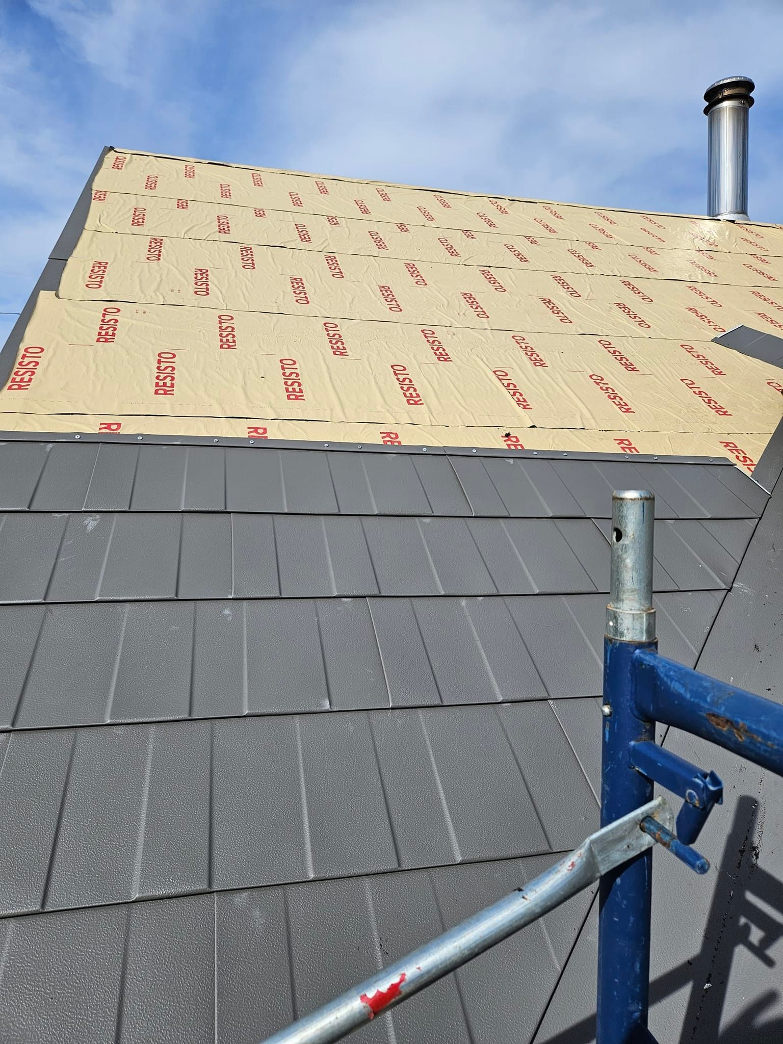 Un toit avec des bardeaux en cours d'installation et un échafaudage devant.