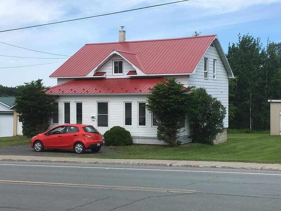 Une voiture rouge est garée devant une maison blanche au toit rouge.