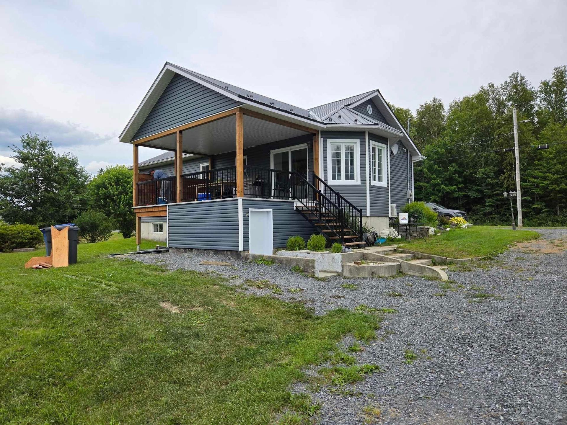 Une petite maison avec un porche et des escaliers est située au sommet d'un champ vert luxuriant.