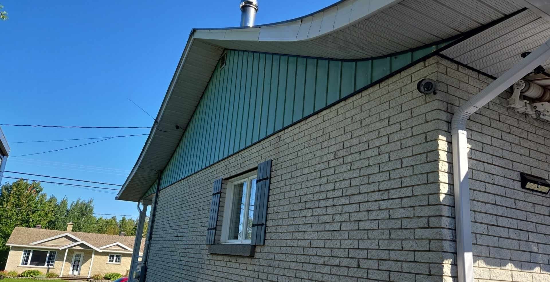 Une maison en briques blanches avec un toit vert et une fenêtre.