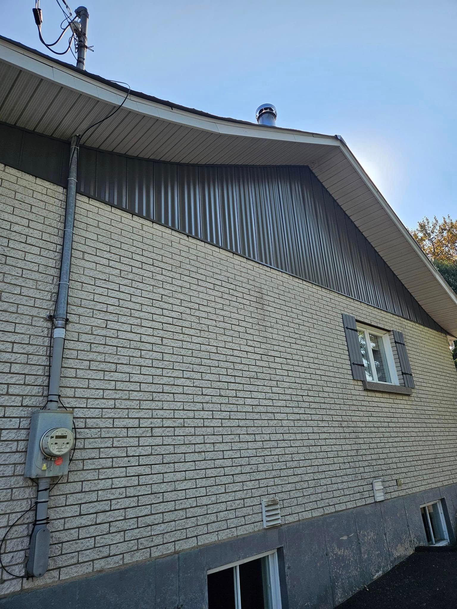 Le côté d'une maison en brique avec un toit et une fenêtre.