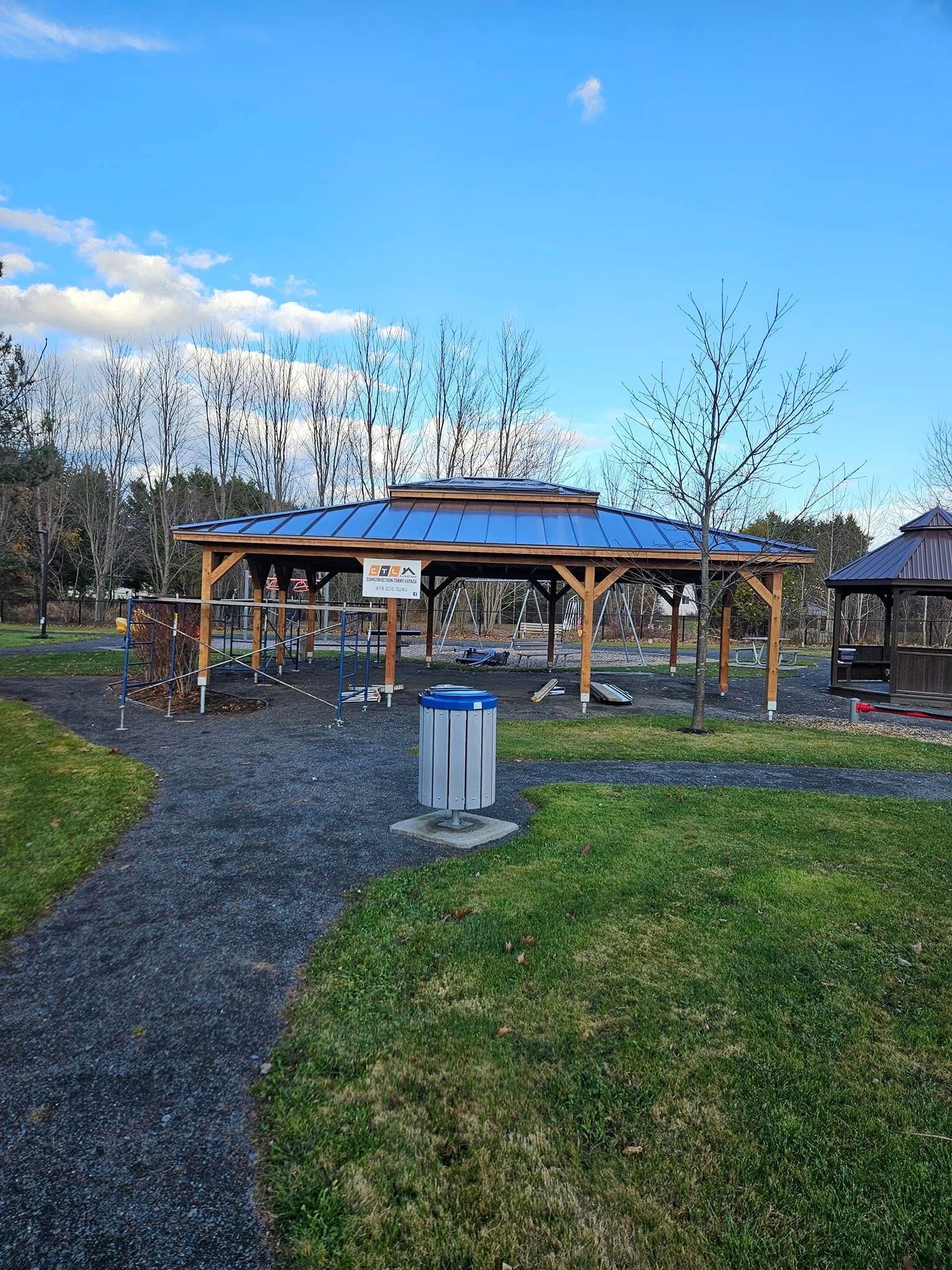 Un belvédère dans un parc avec un toit bleu et une poubelle.