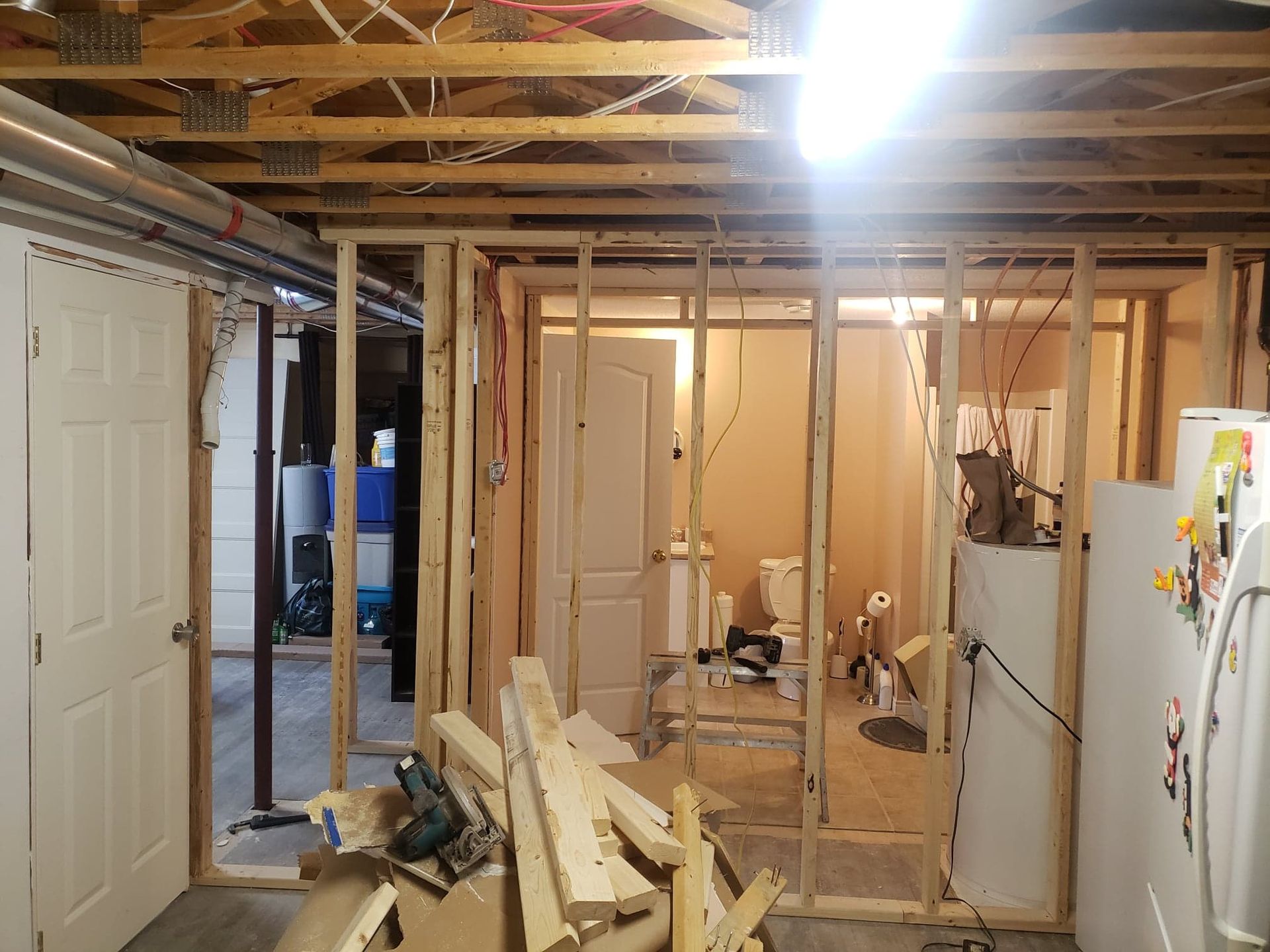 Un sous-sol est en cours de réaménagement avec des poutres en bois et un réfrigérateur.