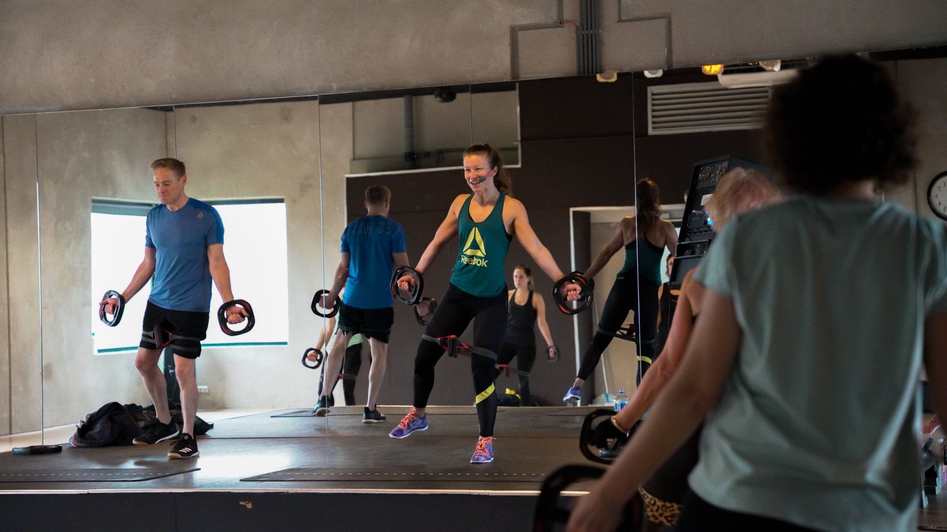 Mensen in een sportschool die trainen met halters en weerstandsbanden. Lachende vrouw in het midden.