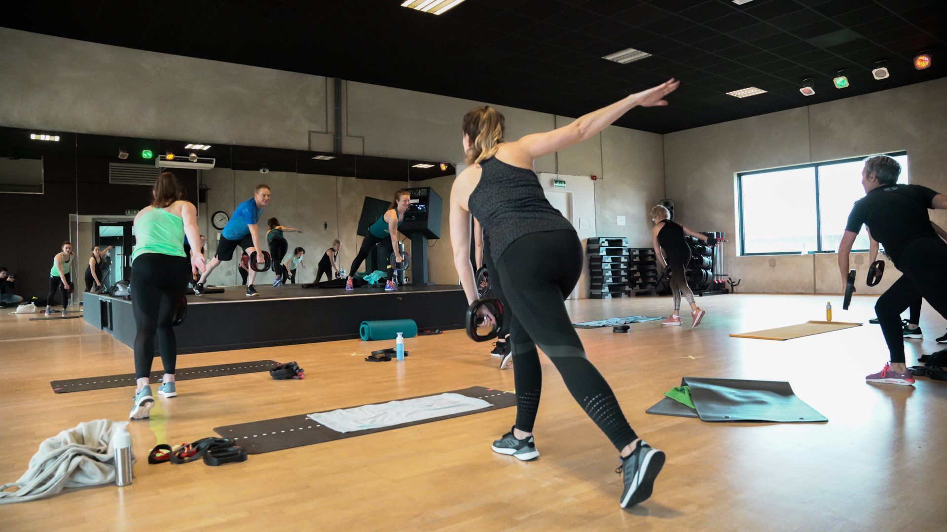 People exercising in a gym. Woman in black activewear reaches arm out during a workout.
