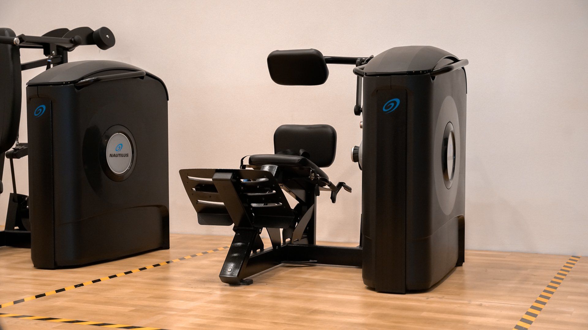 een zwarte fitnessmachine staat op een houten vloer in een sportschool.