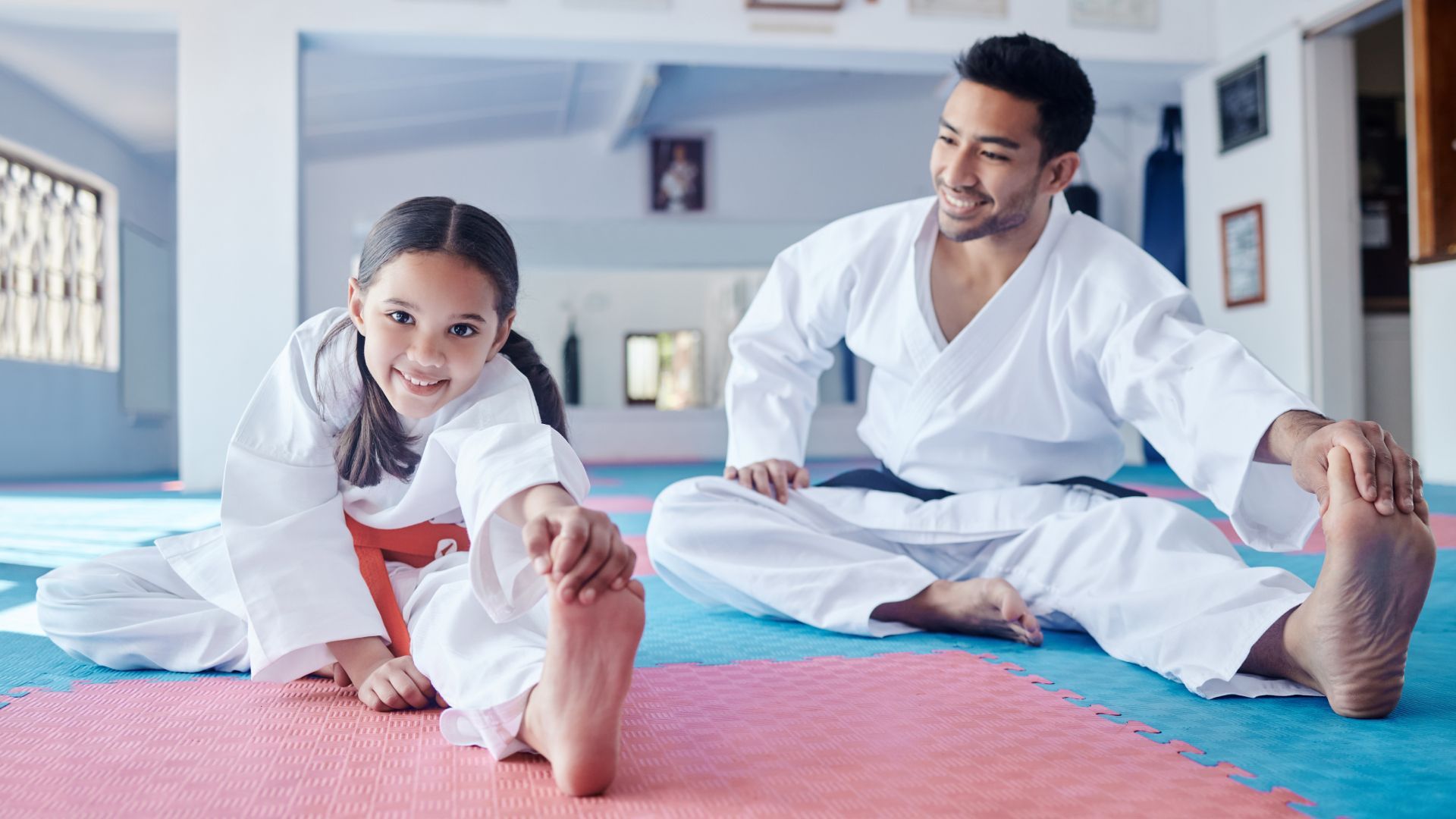 A man and a little girl are stretching on a karate mat.