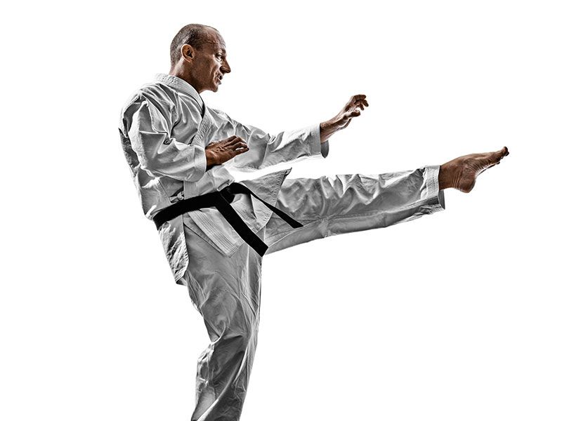 A man in a karate uniform is kicking in the air.