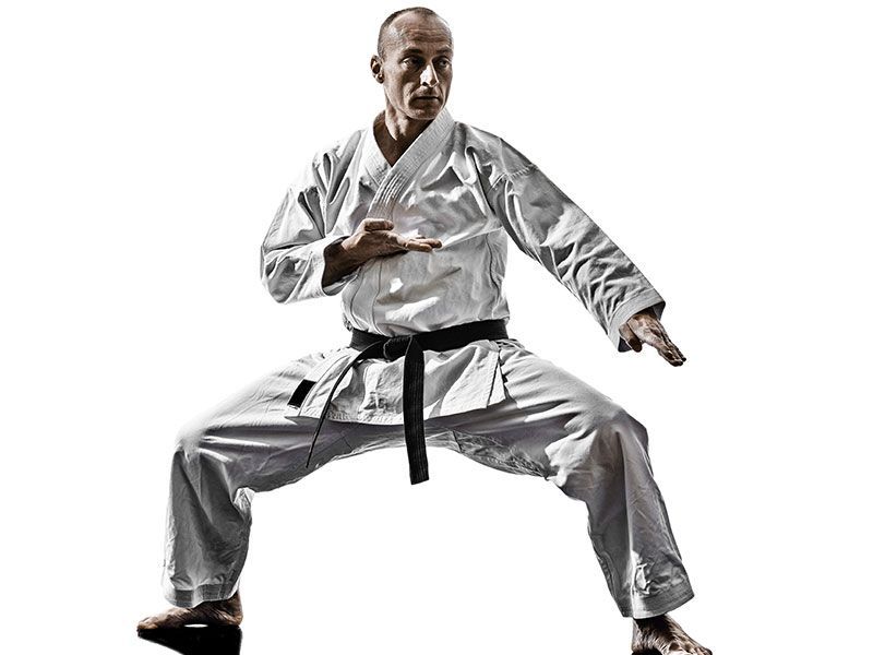 A man in a white karate uniform with a black belt is practicing karate.