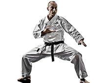 A man in a karate uniform with a black belt is doing a karate pose.