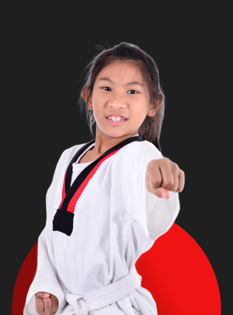 A young girl in a taekwondo uniform is pointing at the camera.
