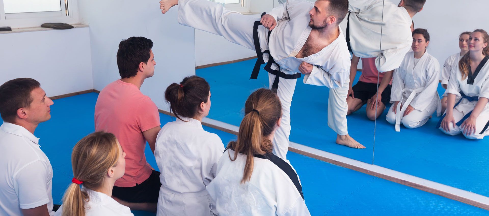 A group of people are watching a man do a kick in a karate class.