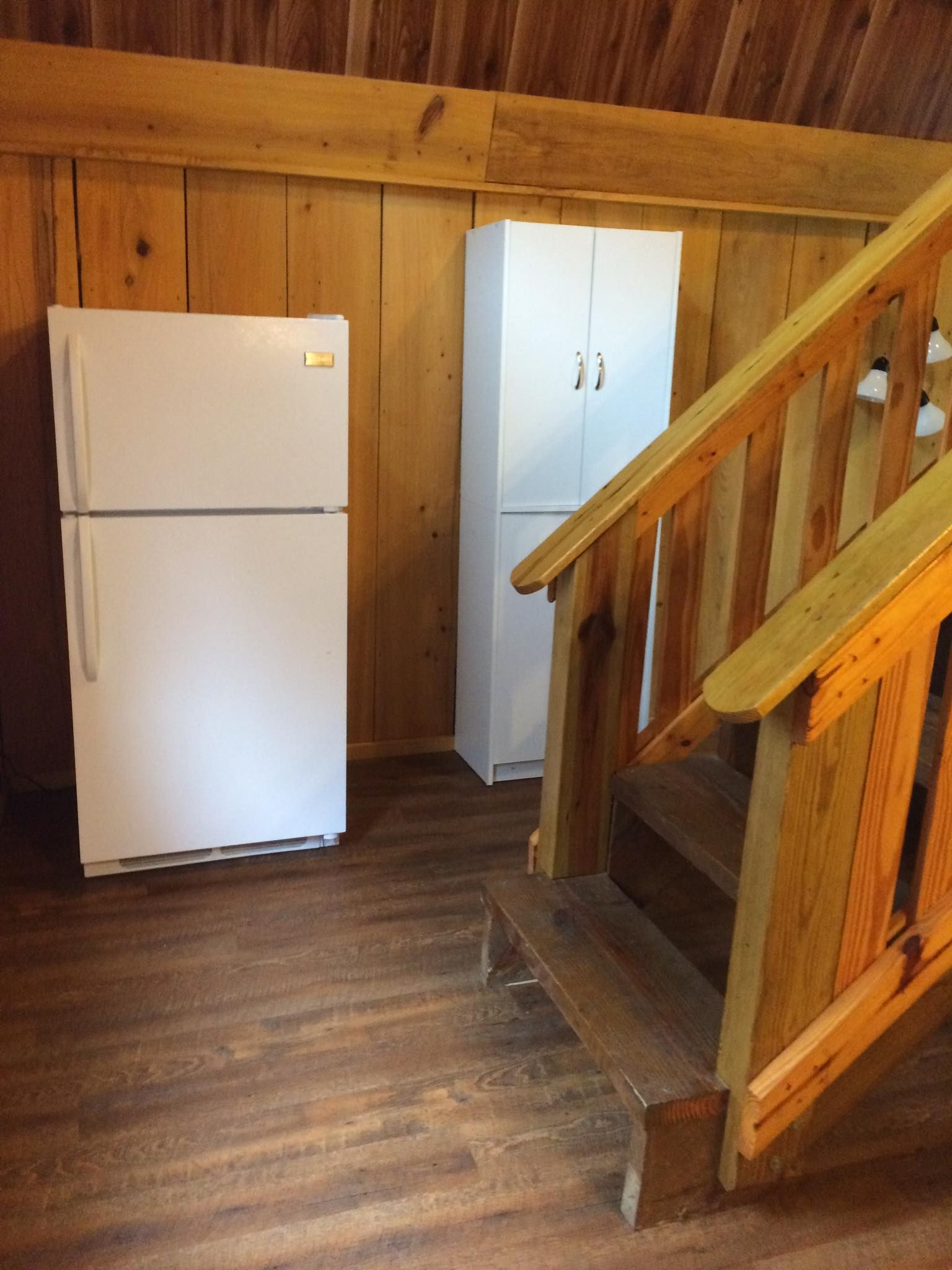 A white refrigerator is in a room next to a wooden staircase