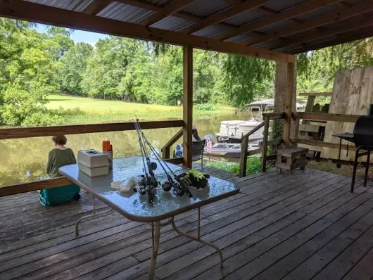 A table with fishing rods on it is on a deck overlooking a lake.