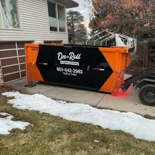 Orange and black dumpster in a driveway next to a house with snow on the ground; 