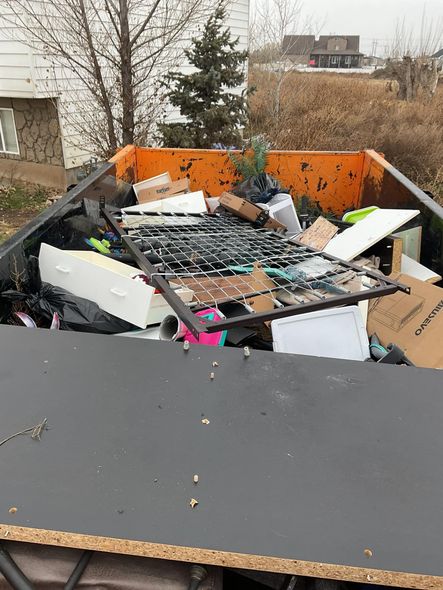 A large, orange dumpster overflowing with discarded furniture, boxes, and debris outside.