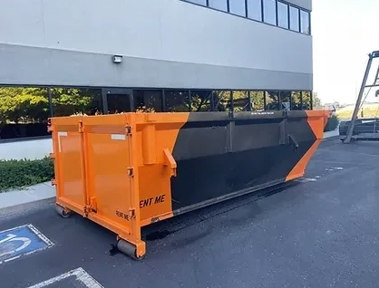 Orange and black dumpster in parking lot, near building.