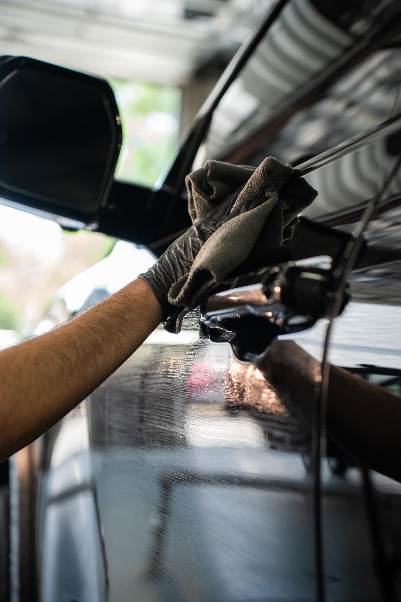 Gloved hand wiping a black car’s side window with a cloth in a garage or car wash