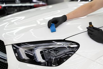 Gloved hands applying protective film to a white car hood near the headlight