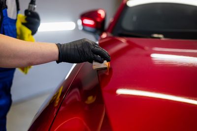 Gloved hand polishing a red car’s hood with a cloth in a garage