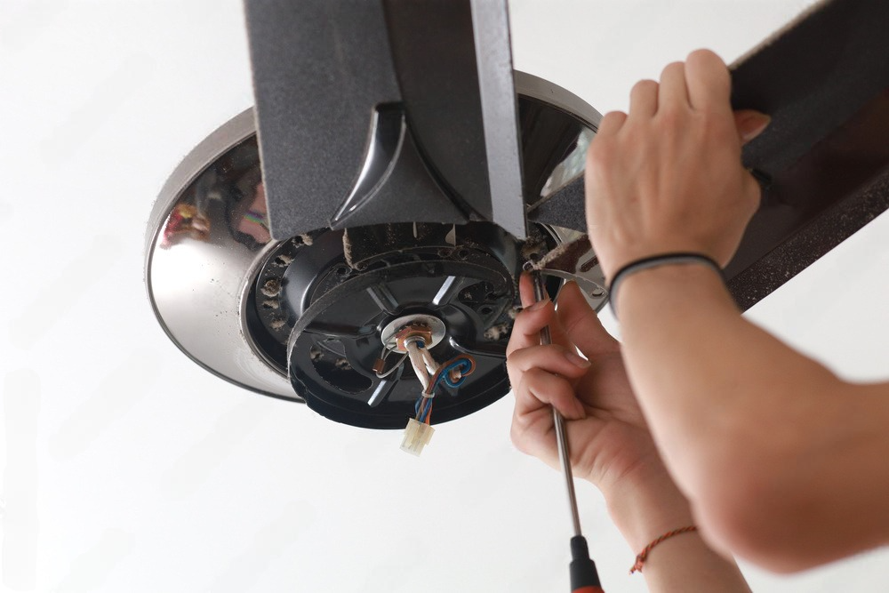 a person is fixing a ceiling fan with a screwdriver