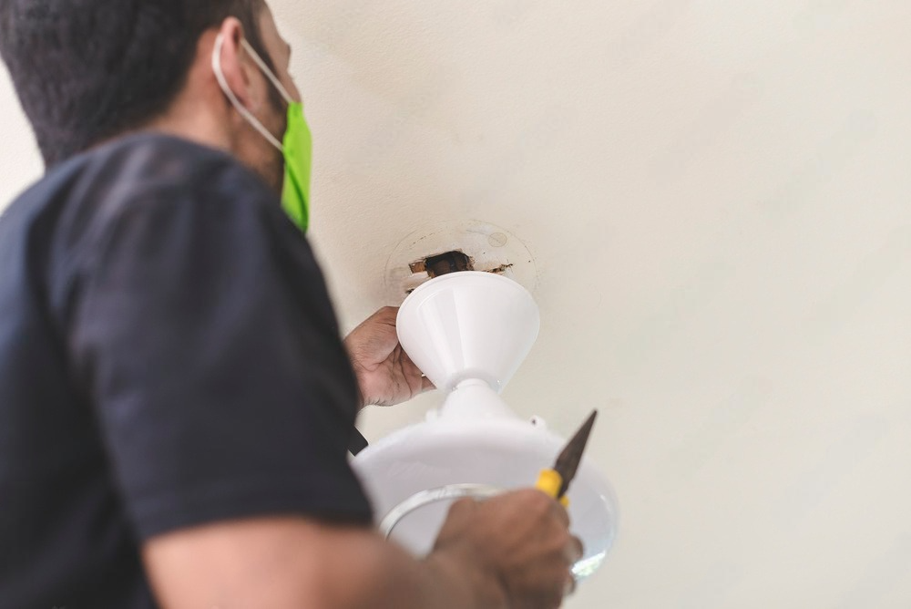 a man wearing a mask is fixing a ceiling fan.