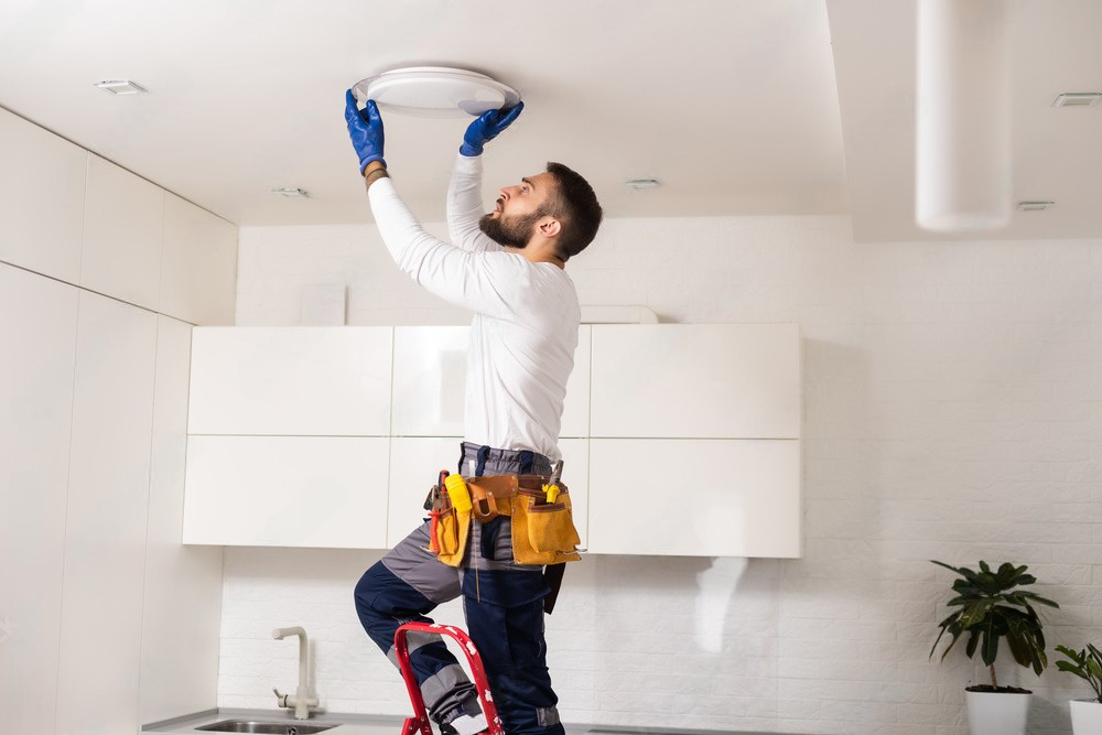 a man is installing a light fixture on the ceiling in a kitchen .