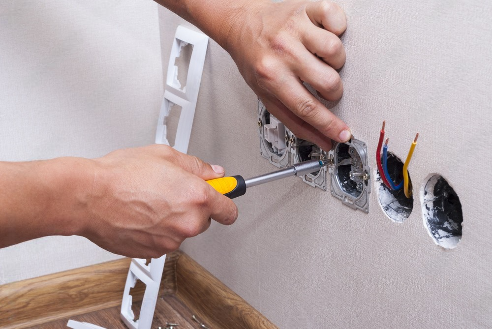 a person is using a screwdriver to install an electrical outlet on a wall .