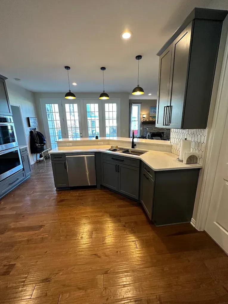 A kitchen with gray cabinets , stainless steel appliances , and hardwood floors.