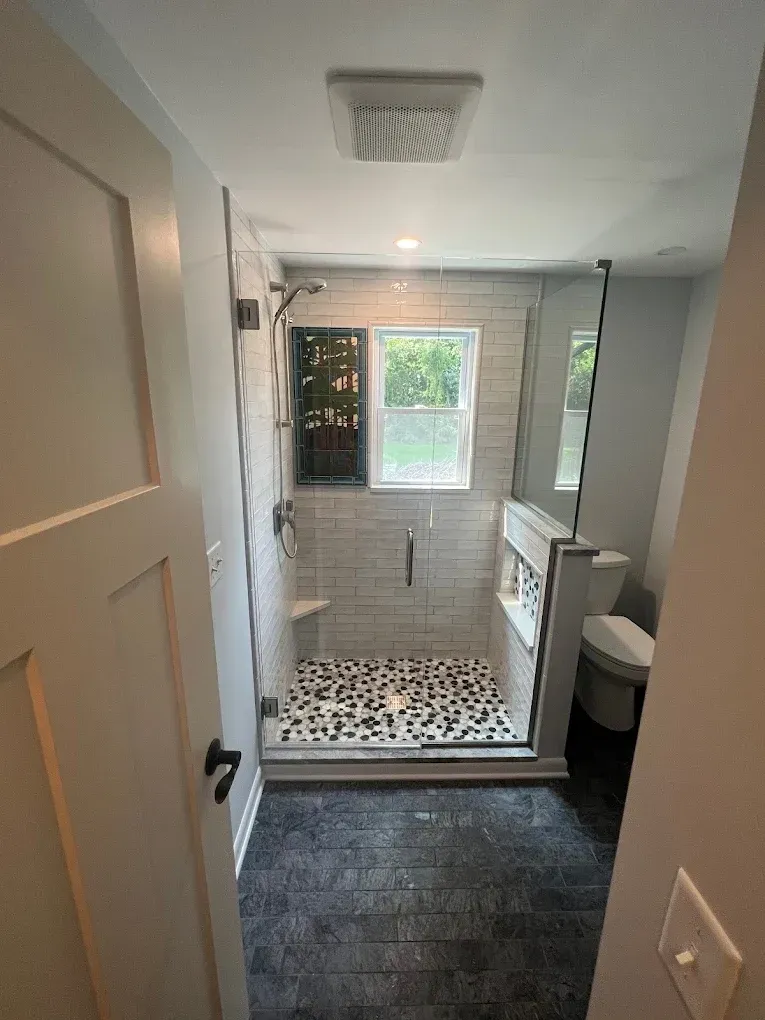 A bathroom with a walk in shower , toilet and window.