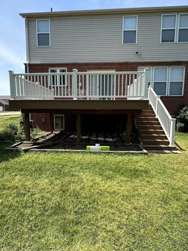 A large deck with stairs leading up to it is in the backyard of a house.