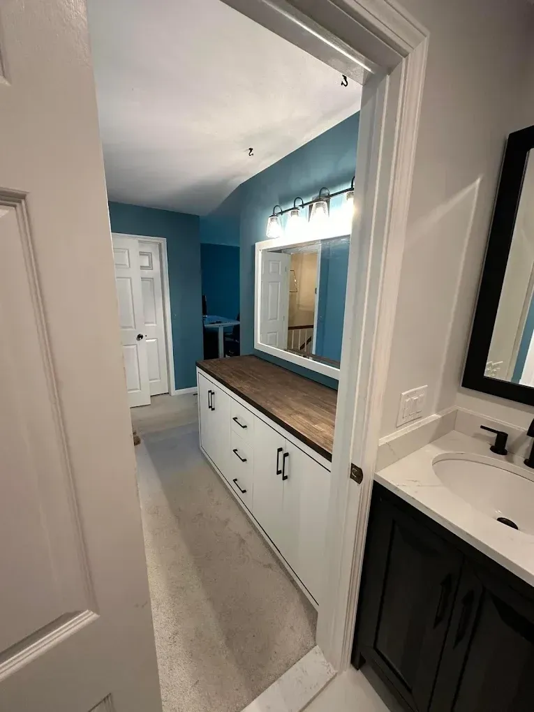 A bathroom with a sink , mirror , cabinets and drawers.