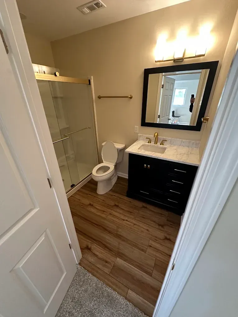 A bathroom with a toilet , sink , mirror and shower.