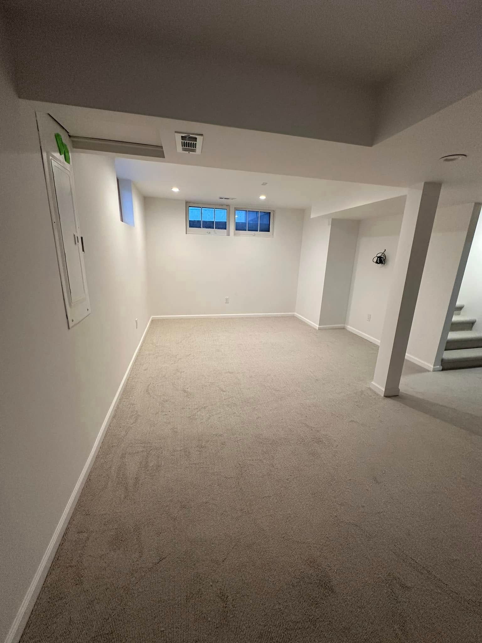 An empty basement with a carpeted floor and white walls.