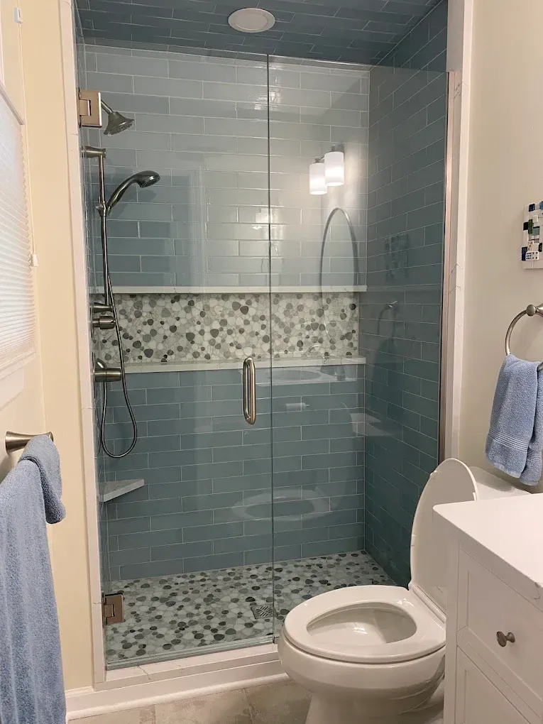 A bathroom with a toilet , sink , shower and blue tiles.