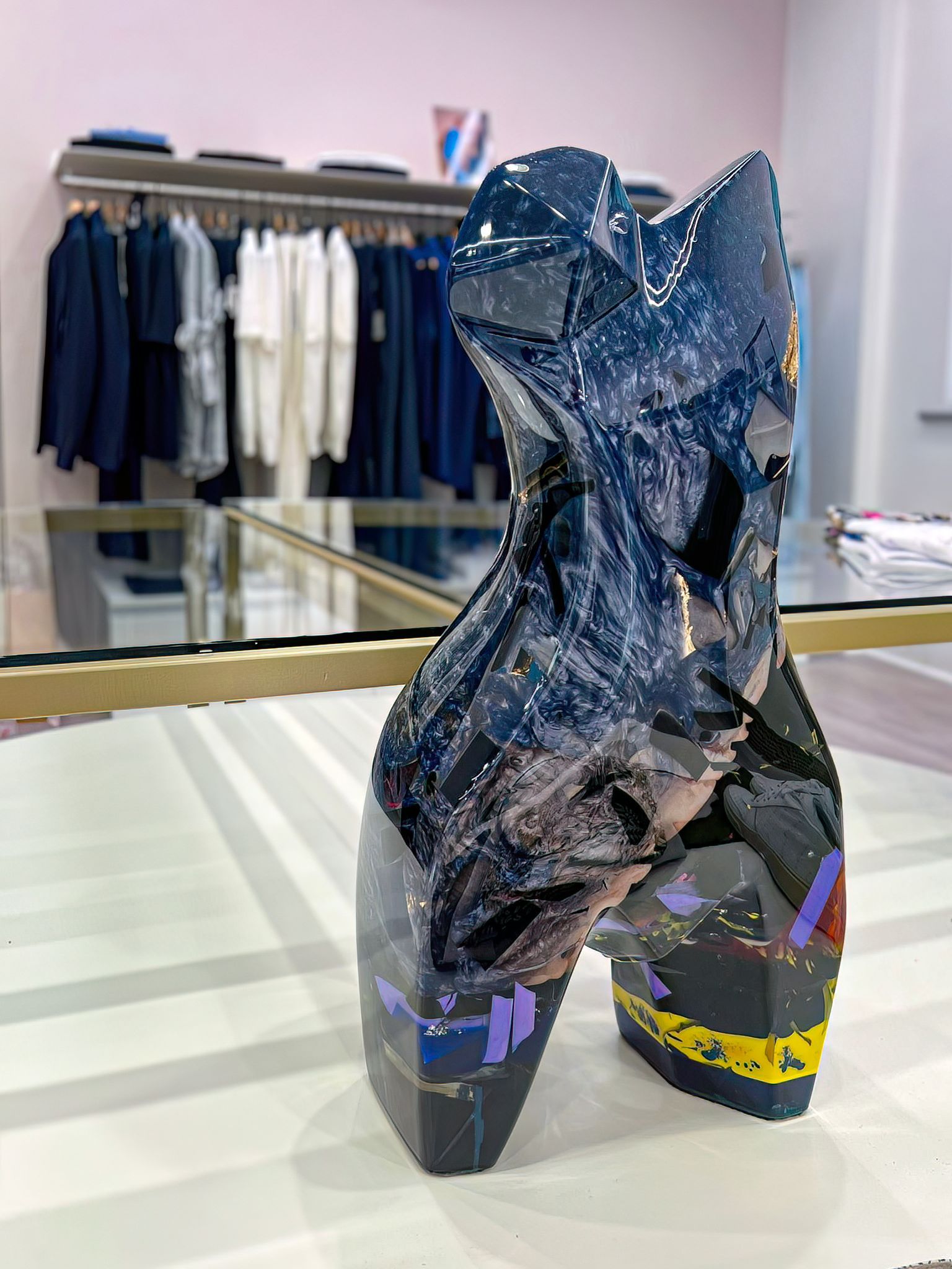 Primo piano della scultura raffigurante un torso femminile, realizzata in resina trasparente e inclusioni policromatiche. Opera con effetto lucido, riflettente, in dettaglio si possono notare le inclusioni multicolore.