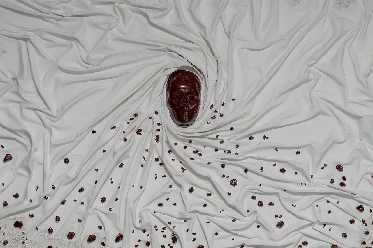 Dettaglio di scultura tridimensionale su pannello di legno raffigurante un volto umano in gesso ceramico color bordeaux e drappeggio contelo resinato. Opera di Guerino Rusconi.